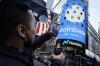 Coinbase employee Daniel Huynh holds a celebratory bottle of champagne as he photographs outside the Nasdaq MarketSite, in New York's Times Square, Wednesday, April 14, 2021. (AP Photo/Richard Drew)