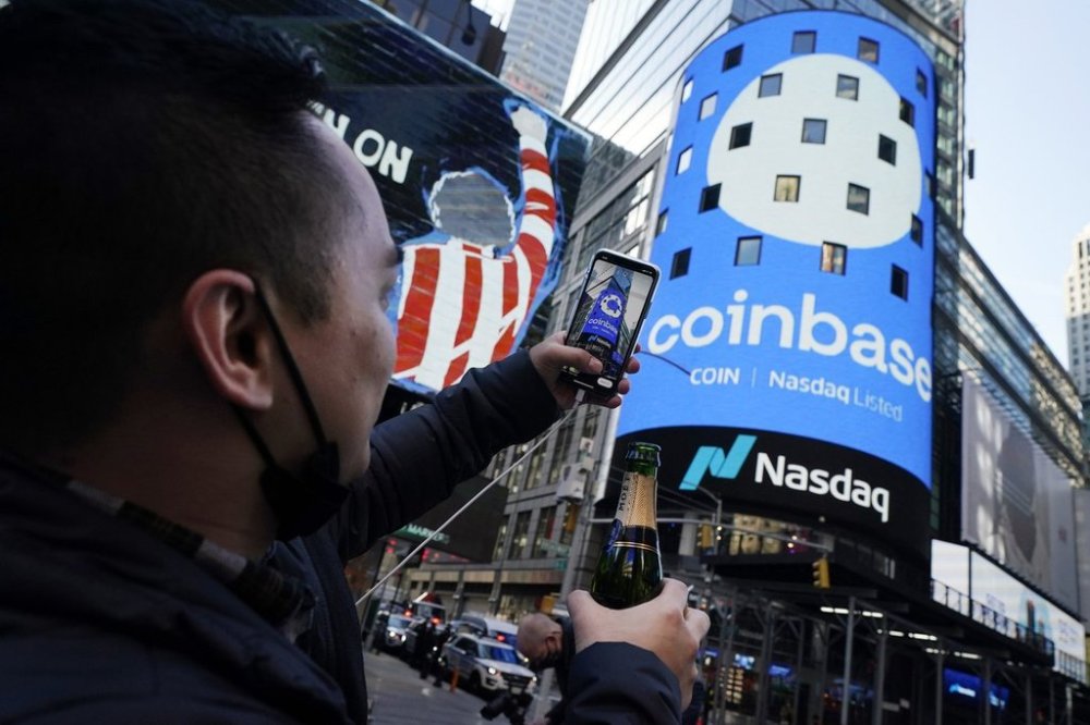 Coinbase employee Daniel Huynh holds a celebratory bottle of champagne as he photographs outside the Nasdaq MarketSite, in New York's Times Square, Wednesday, April 14, 2021. (AP Photo/Richard Drew)