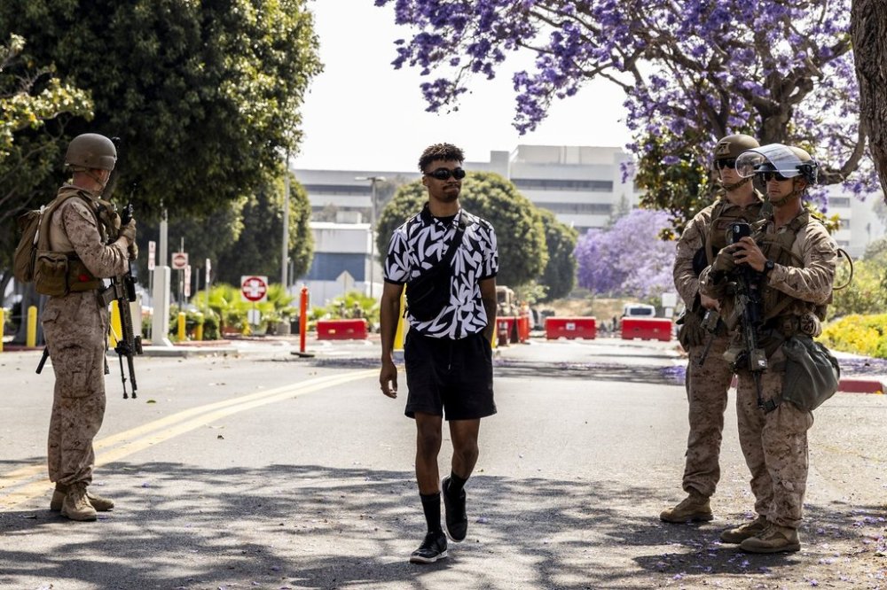 Marcos Leao, center, walks past a checkpoint manned by Marines after he was briefly detained and released for crossing a yellow tape cordon outside the Wilshire Federal Building while trying to get to a Veterans Affairs appointment Friday, June 13, 2025, in Los Angeles. (Stephen Lam/San Francisco Chronicle via AP)