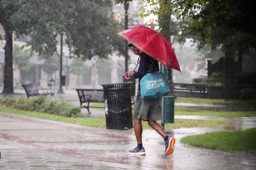 A pedestrian walks along a street during a rain shower Tuesday, July 15, 2025, in Orlando, Fla., as tropical weather moves over the state. (AP Photo/John Raoux)