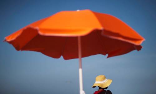 FILE - In this Tuesday, June 16, 2015, file photo, a woman sits next to an umbrella while looking out toward the ocean in Folly Beach, S.C. That sunscreen in your bag may not protect your skin as much as you think. Even after regulators updated standards for labeling sunscreen in 2012, tests have shown many provide far less protection than advertised. If you&rsquo;re going to be outside, experts recommend finding some shade and wear clothing that covers your arms and legs, and a broad-brimmed hat to protect your face, ears and neck. (AP Photo/David Goldman, File)