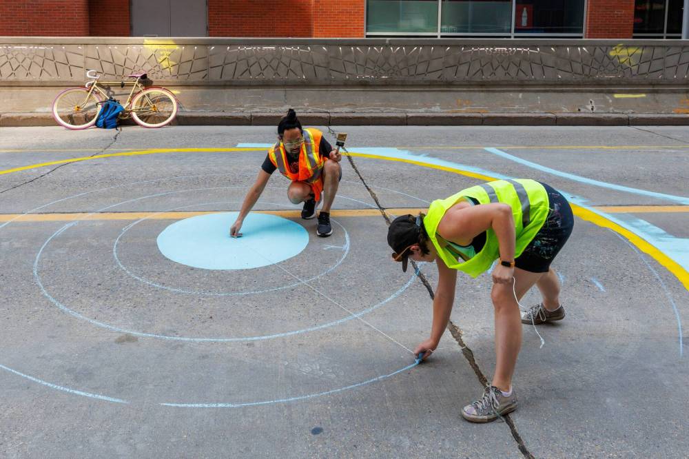 MIKE DEAL / FREE PRESS Artist, Alex Plante (green highviz), with a little help from Takashi Iwasaki (artistic lead) creating one of several murals along a four-block stretch of Graham between Carlton and Garry Street Tuesday morning. 250708 - Tuesday, July 08, 2025.