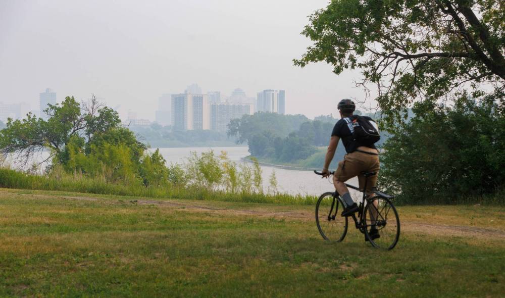 MIKE DEAL / FREE PRESS
Wildfire smoke shrouds downtown high-rises as a cyclist makes their way along a bike path beside the Red River Friday morning.