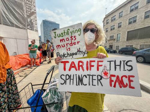 SCOTT BILLECK / FREE PRESS
                                Ann LeTouche holds a pair of signs, protesting a visit from U.S. Ambassador Peter Hoekstra at the Winnipeg Art Gallery on Tuesday. LeTouche fears what she calls American imperialism and a trend toward fascism south of the border and is worried will spread north of it if Canada is not careful. Protestors outside the Winnipeg Art Gallery (WAG) wave signs as U.S. ambassador Pete Hoekstra speaks to members of the Winnipeg Chamber of Commerce over the noon-hour Tuesday. 250729 - Tuesday, July 29, 2025.