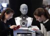People check their phones as AMECA, an AI robot, looks on at the All In artificial intelligence conference, on Sept. 28, 2023 in Montreal. THE CANADIAN PRESS/Ryan Remiorz