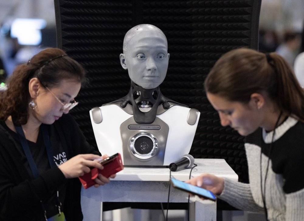 People check their phones as AMECA, an AI robot, looks on at the All In artificial intelligence conference, on Sept. 28, 2023 in Montreal. THE CANADIAN PRESS/Ryan Remiorz