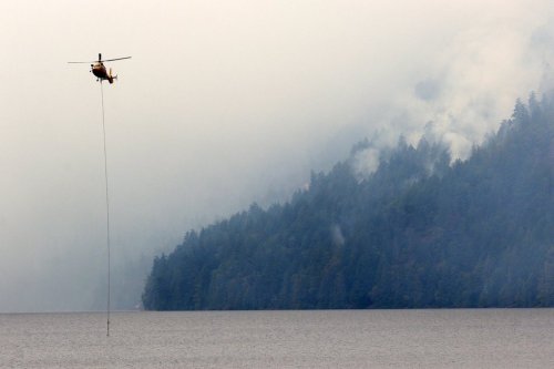 A helicopter refills a bucket of water at Cameron Lake off Highway 4 where the Wesley Ridge wildfire continues to burn out-of-control near Coombs, B.C., on Sunday, Aug. 3, 2025. THE CANADIAN PRESS/Chad Hipolito