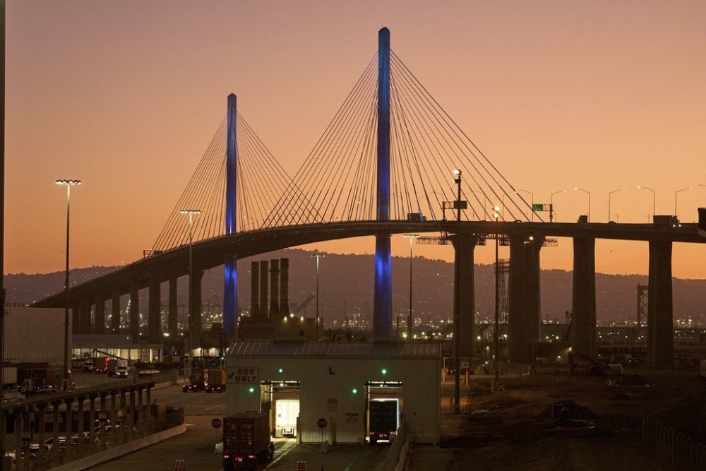 Trucks transporting containers undergo X-ray scanning at entry gates at the Long Beach Container Terminal (LBCT), one of the most advanced, fully automated container terminals in the U.S., with the the Long Beach International Gateway Bridge in the background at the Port of Long Beach, Calif., Thursday, July 31, 2025. (AP Photo/Damian Dovarganes)