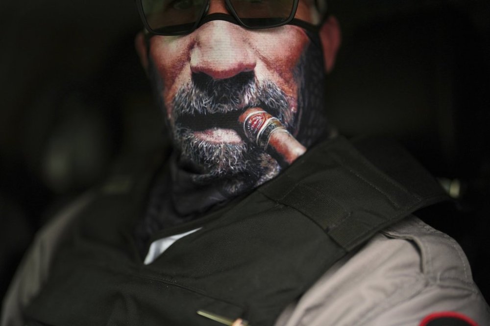 An immigration official wears a face mask depicting a cigar and beard as he waits to transport detained immigrants Wednesday, July 23, 2025, in Baldwin Park, Calif. (AP Photo/Gregory Bull)
