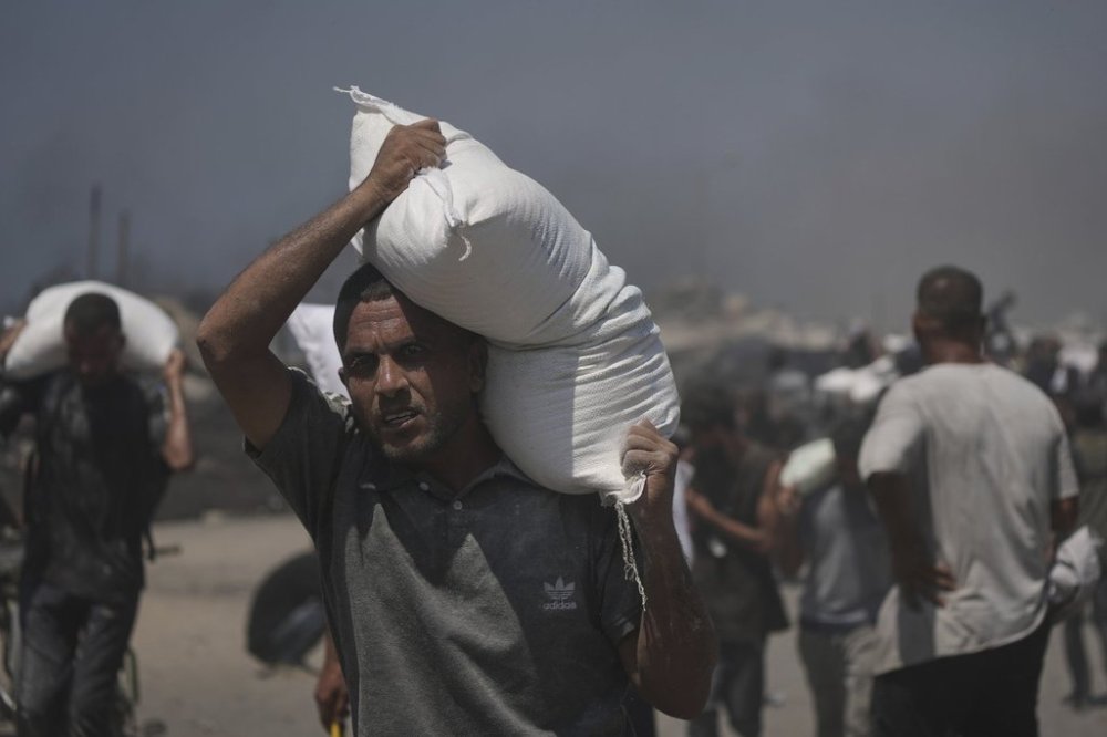 Palestinians carry sacks of flour unloaded from a humanitarian aid convoy that reached Gaza City from the northern Gaza Strip, Sunday, July 27, 2025. (AP Photo/Jehad Alshrafi)