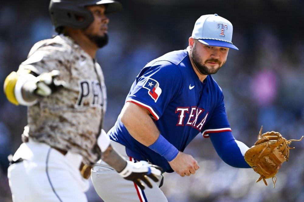 Texas Rangers first baseman Jake Burger, right, cannot make the tag on San Diego Padres' Luis Arraez, left, on a single during the second inning of a baseball game Friday, July 4, 2025. (AP Photo/Denis Poroy)