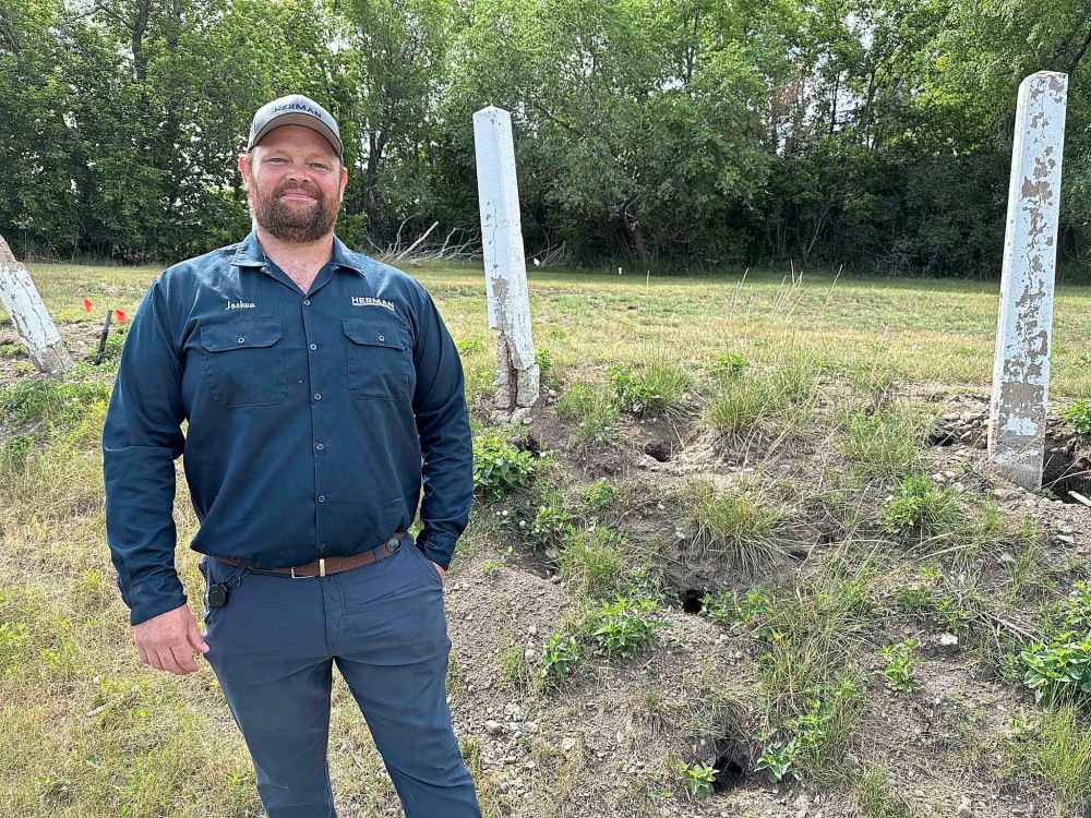 Joshua Herman, owner/operator of Herman Pest Control Services, poses for a photo on Monday, July 14, 2025, next to holes dug by Richardson's ground squirrels in Minot, N.D. (AP Photo/Jack Dura)