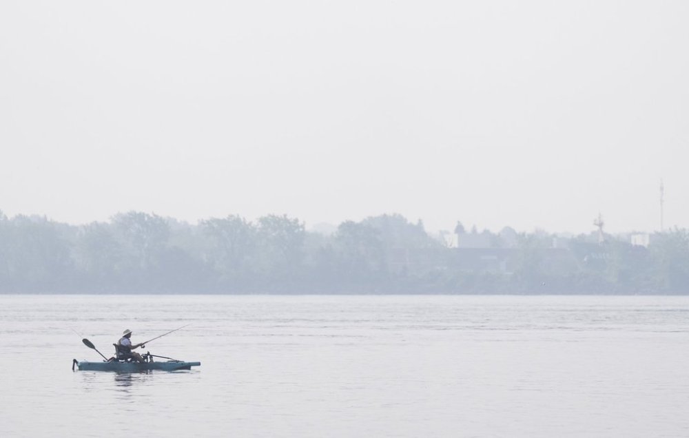 A man fishes on Lake St. Louis, Friday, June 30, 2023 in Lachine, Que. Environment Canada says forest fires are causing poor air quality today across much of the country, including Quebec. THE CANADIAN PRESS/Christinne Muschi