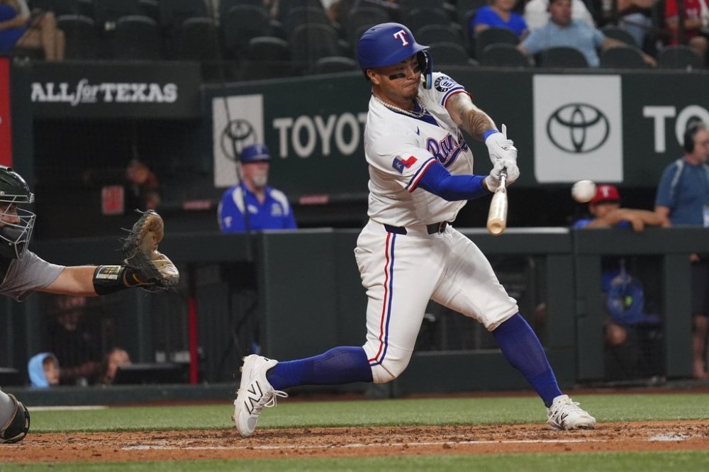 Texas Rangers' Cody Freeman, right, hits a double, that scored teammate Josh Smith, in front of Athletics catcher Shea Langeliers, left, during the fifth inning of a baseball game, Monday, July 21, 2025, in Arlington, Texas. (AP Photo/LM Otero)