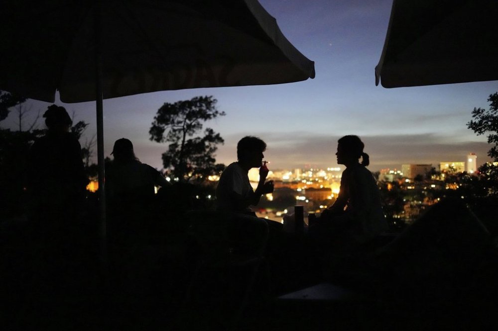 FILE - People sit on the terrace of a closed bar at the Monte Agudo viewpoint overlooking Lisbon during a nationwide power outage, Monday, April 28, 2025. (AP Photo/Armando Franca, file)