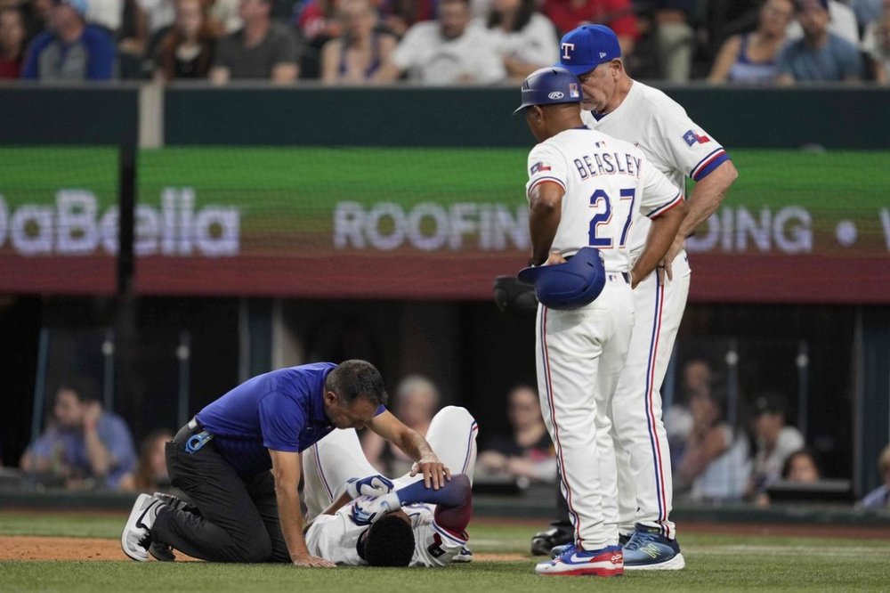 Texas Rangers athletic trainer Matt Lucero, left, third base coach Tony Beasley (27) and manager Bruce Bochy, right, check on Marcus Semien (2) after Semien was hit by a pitch in the third inning of a baseball game against the Atlanta Braves Saturday, July 26, 2025, in Arlington, Texas. (AP Photo/Tony Gutierrez)