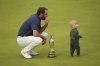 Scottie Scheffler of the United States holds the Claret Jug trophy as his son Bennett stands on the 18th green after winning the British Open golf championship at the Royal Portrush Golf Club, Northern Ireland, Sunday, July 20, 2025. (AP Photo/Francisco Seco)