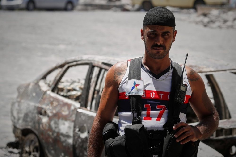 A Druze militiaman poses for a picture next to a burned-out car following last week's sectarian clashes in the Druze-majority town of Sweida, Syria, Friday, July 25, 2025. (AP Photo/Omar Sanadiki)
