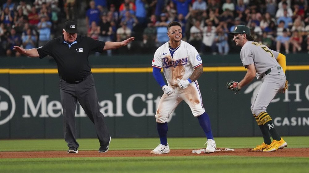 Texas Rangers' Cody Freeman, center, reacts in front of Athletics shortstop Jacob Wilson (5) at second base after hitting a double that scored teammate Josh Smith during the fifth inning of a baseball game, Monday, July 21, 2025, in Arlington, Texas. (AP Photo/LM Otero)