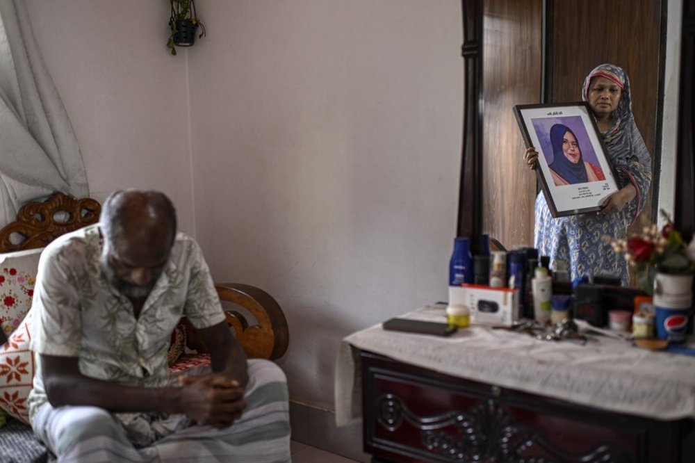 Asma Begum, standing next to her husband, is reflected in a mirror as she holds a portrait of her daughter Meherunnesa, who died by a stray bullet while standing near a window at her home, hours after former Prime Minister Sheikh Hasina fled the country amid a student-led mass uprising last year in Dhaka, Bangladesh, July 28, 2025. (AP Photo/Mahmud Hossain Opu)