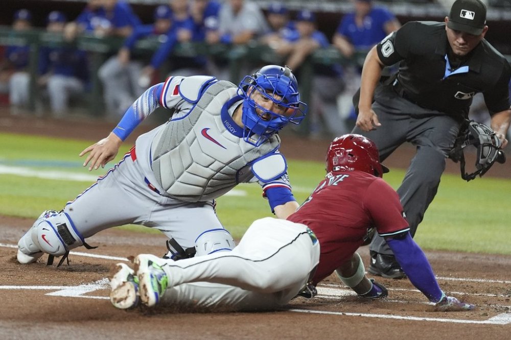 Texas Rangers catcher Kyle Higashioka, left, tags out Arizona Diamondbacks' Ketel Marte at home plate as home plate umpire Roberto Ortiz, right, looks on during the first inning of a baseball game Wednesday, Sept. 3, 2025, in Phoenix. (AP Photo/Ross D. Franklin)