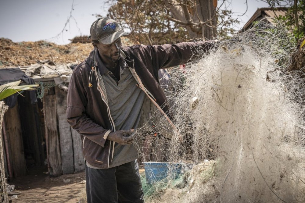 Famara Nudure, a fisherman for more than 40 years, inspects what is left of his fishing nets which were damaged at sea by trawlers, in Gunjur, Gambia, on March 23, 2025. (AP Photo/Grace Ekpu)