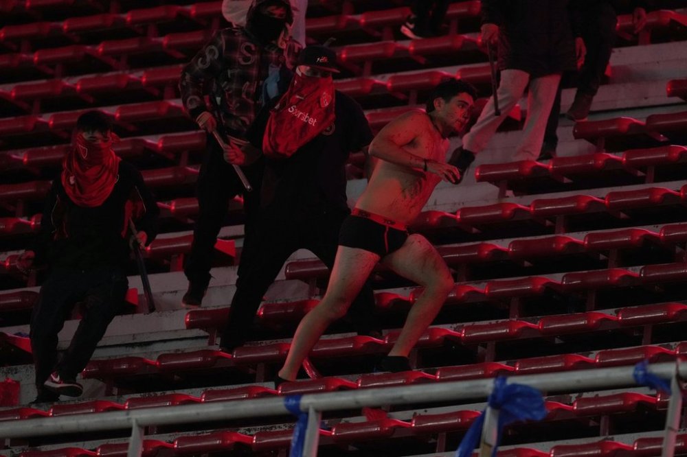 Fans of Argentina's Independiente attack a Universidad de Chile fan, right, after they stripped him of his clothing during a Copa Sudamericana round of sixteen second leg soccer match at the Libertadores de America stadium in Avellaneda, Argentina, Wednesday, Aug. 20, 2025. (AP Photo/Gustavo Garello)