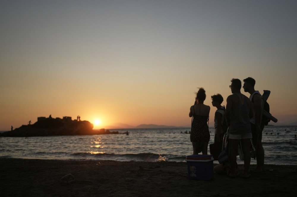 A family enjoys sunset in southern Athens, Greece, Monday, Aug. 11, 2025. (AP Photo/Thanassis Stavrakis)
