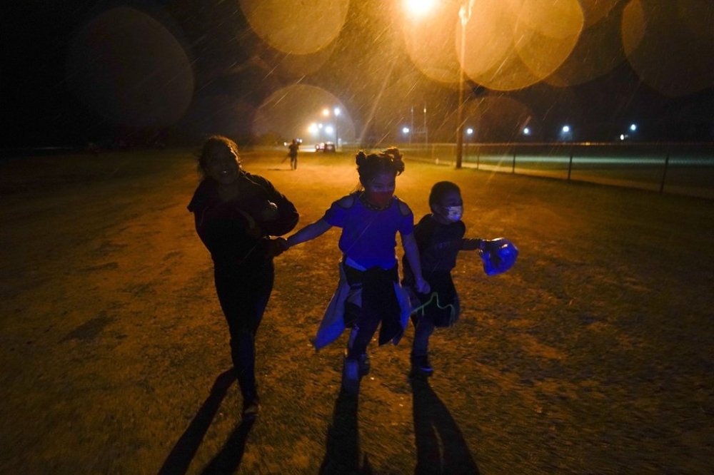 FILE - Young migrants hold hands as they run in the rain at an intake area after turning themselves in upon crossing the U.S.-Mexico border in Roma, Texas, May 11, 2021. (AP Photo/Gregory Bull, File)