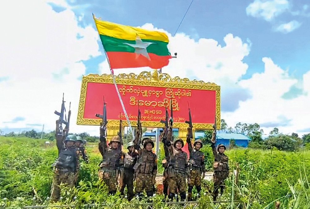 Army soldiers pose in front of the sign for the town of Demoso in Myanmar's eastern state of Kayah, which the military government claimed to have recaptured from resistance forces on Tuesday, Aug. 19, 2025 (Myanmar Military via AP)