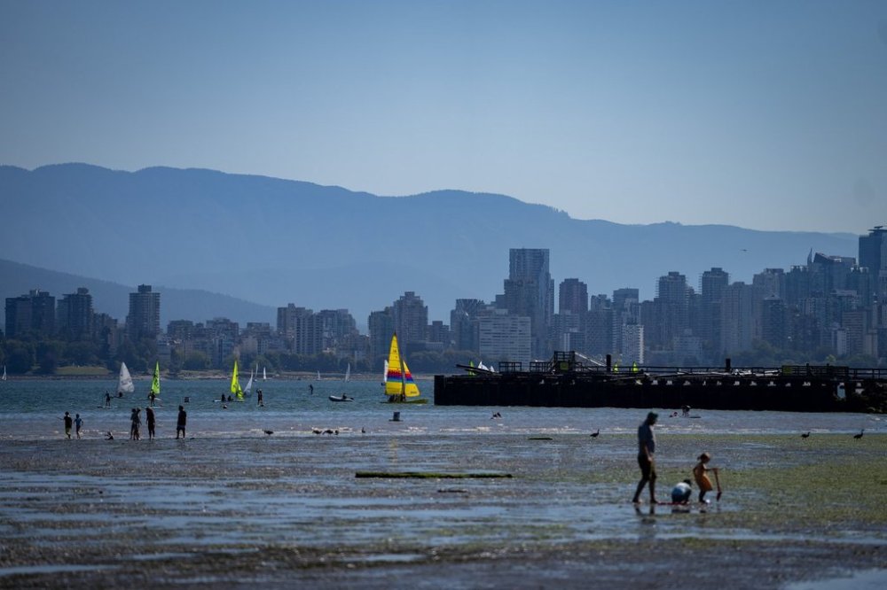 People walk on the beach during low tide as sailboats pass in Vancouver, Sunday, July 7, 2024. Heat warnings have been put in place for the Metro Vancouver area for elevated temperatures. THE CANADIAN PRESS/Ethan Cairns