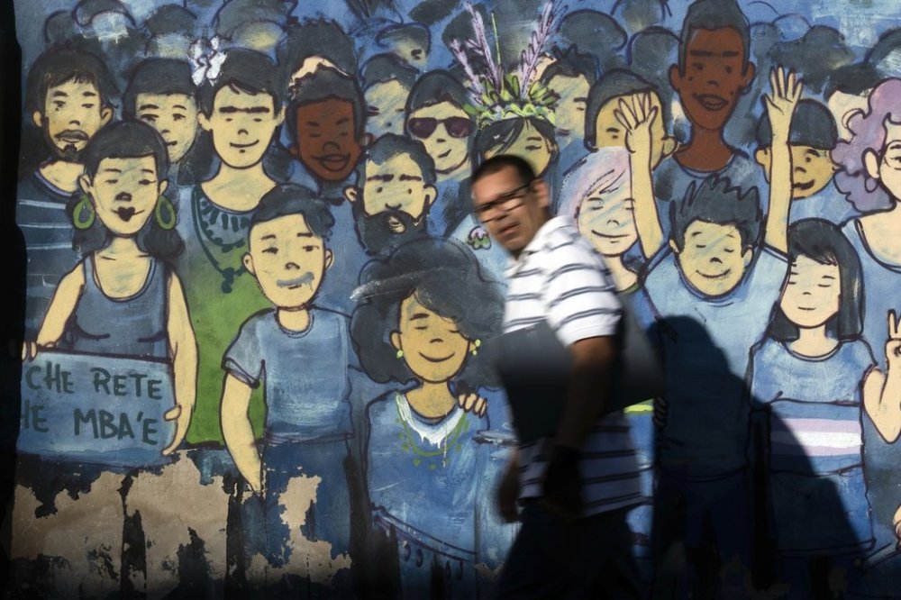 A pedestrian passes a mural that rads in the Guarani language