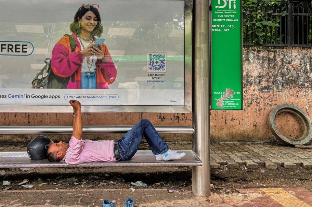 A commuter watches a video on his mobile phone lying down at a bus stop in New Delhi, India, Tuesday, Aug. 12, 2025. (AP Photo/Manish Swarup)
