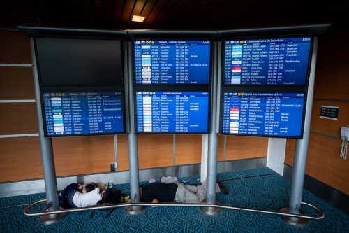 People sleep under a flight information board at the Vancouver International Airport in Richmond, B.C., Saturday, Aug. 16, 2025. THE CANADIAN PRESS/Ethan Cairns