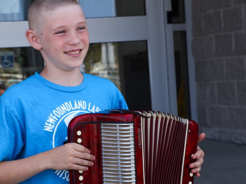 Ten-year-old Zander Wright is shown holding his accordion outside a reception centre for people evacuated from a fire near St. John's, N.L., on Wednesday, Aug. 13, 2025. He donated the $121 he raised by busking to help the people inside. THE CANADIAN PRESS/Elling Lien