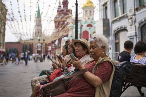 FILE - People look at their phones near the Kremlin in Moscow, July 16, 2025. (AP Photo/Alexander Zemlianichenko, File)