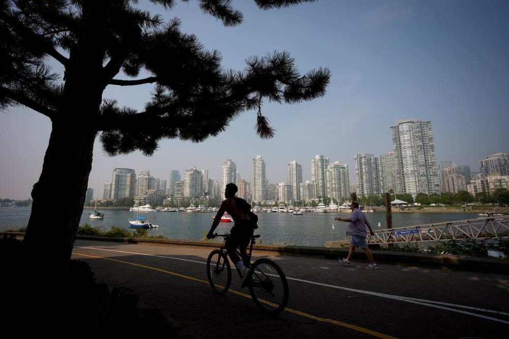 A cyclist is silhouetted while a pedestrian walks on the False Creek seawall as smoke from wildfires burning in B.C. and the U.S. hangs in the air, in Vancouver, B.C., Wednesday, Sept. 3, 2025. THE CANADIAN PRESS/Darryl Dyck