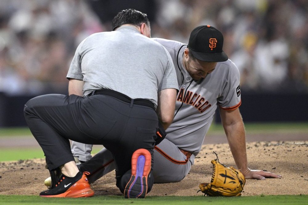 San Francisco Giants starting pitcher Landen Roupp, right, is checked by a trainer after being hit by a line drive during the third inning of a baseball game against the San Diego Padres Wednesday, Aug. 20, 2025, in San Diego. (AP Photo/Orlando Ramirez)