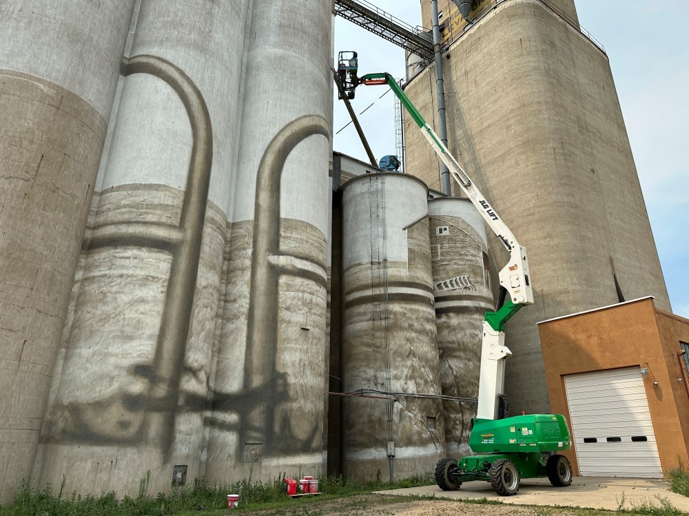 Artist Guido van Helten uses a boom lift to ascend the side of silos where he is painting a mural on Monday, July 14, 2025, in Minot, N.D. (Jack Dura/Guido van Helten via AP)