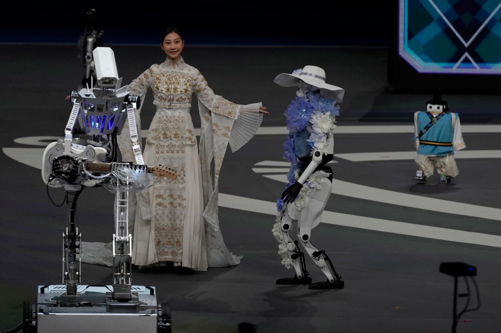 A model poses near robots during the opening ceremony of the World Humanoid Robot Games held in Beijing, China, Thursday, Aug. 14, 2025. (AP Photo/Ng Han Guan)