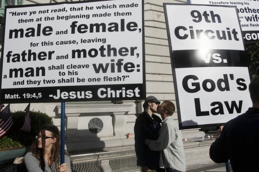 FILE - Aiden Lougee, center left, kisses his boyfriend, Rex Resa, seen between signs held by opponents to gay marriage outside of the courthouse after a hearing in the Ninth Circuit Court of Appeals, Monday, Dec. 6, 2010, in San Francisco. (AP Photo/Jeff Chiu, File)