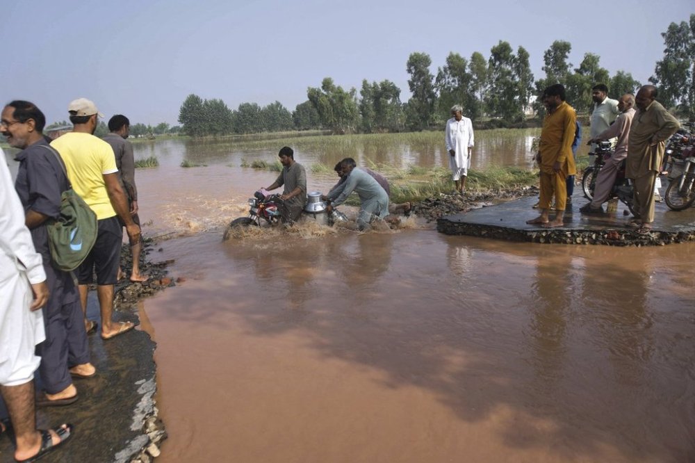 Villagers help a milkman crossing the flooded portion of a road damaged by floods after torrential rains on the outskirts of Sodhra town, in Wazirabad district, Pakistan, Friday, Aug. 29, 2025. (AP Photo/A. Rizvi)
