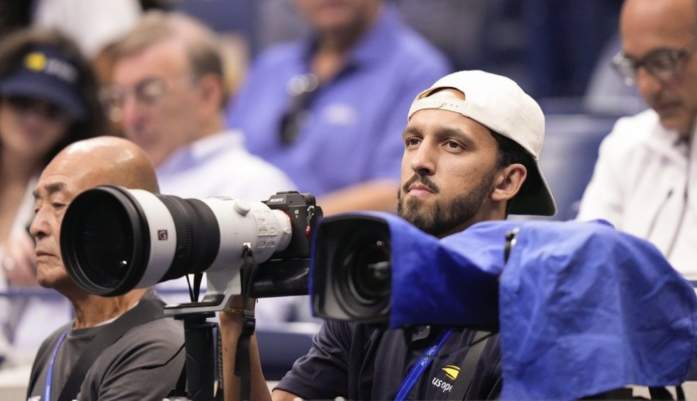 Landry Shamet, right, prepares to photograph the men's singles final between Jannik Sinner, of Italy, and Carlos Alcaraz, of Spain, at the U.S. Open tennis championships, Sunday, Sept. 7, 2025, in New York. (AP Photo/Yuki Iwamura)