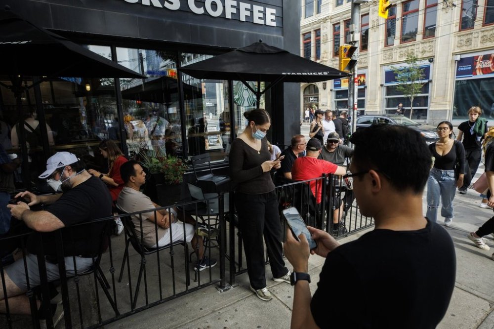 Canada's telecommunications regulator is mandating service providers to notify it and other government authorities within two hours when they experience major network outages. People use electronics outside a coffee shop in Toronto amid a nationwide Rogers outage, affecting many of the telecommunication company's services, Friday, July 8, 2022. THE CANADIAN PRESS/Cole Burston