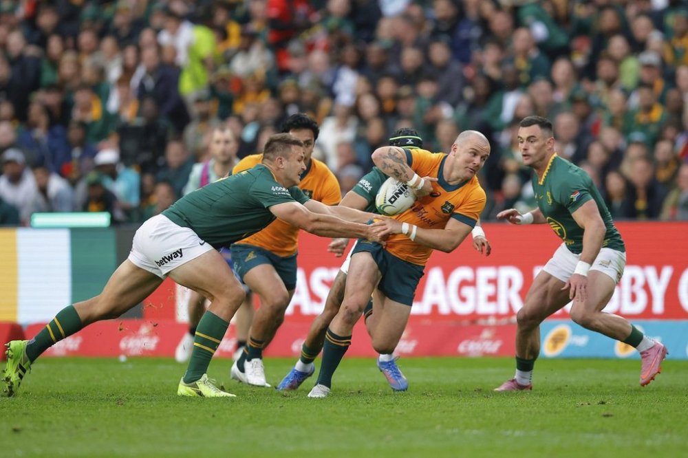 Australia's Dylan Pietsch, centre, being tackled by South Africa's Andre Esterhuizen, left, during a rugby championship test match between South Africa and Australia, at Ellis Park stadium in Johannesburg, South Africa, Saturday, Aug. 16, 2025. (AP Photo/Frans Lombard)