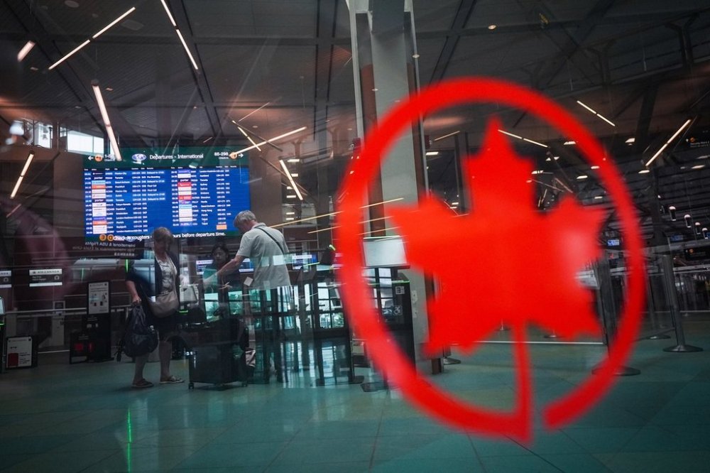 Seen through a barrier with an Air Canada logo on it, passengers check in for an international Air Canada flight at Vancouver International Airport, in Richmond, B.C., on Wednesday, August 13, 2025. THE CANADIAN PRESS/Darryl Dyck