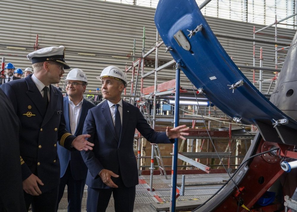 Prime Minister Mark Carney, right, and ThyssenKrupp Marine Systems CEO Oliver Burkhardt, centre, speak with Captain Jeremy in front of a 212A class submarine under maintenance as they tour the submarine building facility in Kiel, Germany on Tuesday, Aug. 26, 2025. THE CANADIAN PRESS/Christinne Muschi