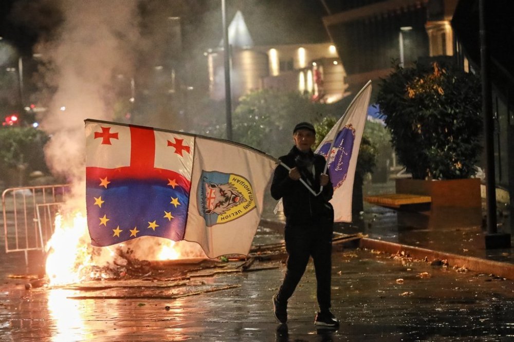 A demonstrator with a Georgian national, EU and other flags walks in front of police line during an opposition rally in the city center of Tbilisi, Georgia, on Saturday, Oct. 4, 2025, boycotting the municipal elections and calling for the release of political opponents. (AP Photo/Zurab Tsertsvadze)