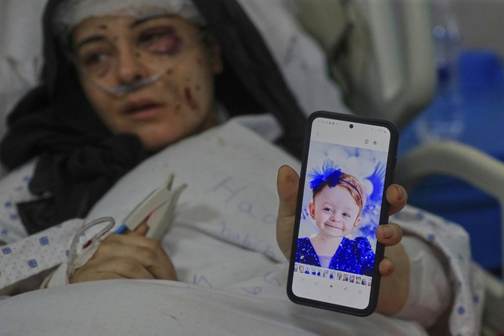 Amani Bazzi, who was injured Sunday in the town of Bint Jbeil, shows a portrait of one her three kids who were killed after an Israeli drone strike hit her family car, as she lies in Tibnin hospital, southern Lebanon, Monday, Sept. 22, 2025. (AP Photo/Mohammed Zaatari)