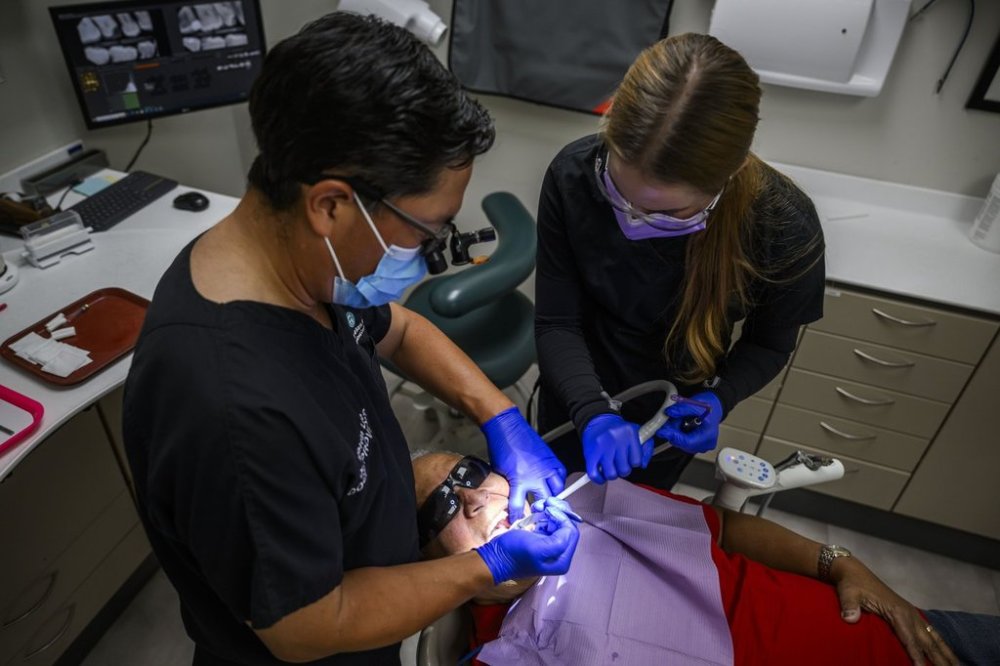 Dr. Melvin Lee, left, performs a tooth extraction for patient Robert McFarlane, as team member Sofia Christow-Filleul assists, at his dental clinic in Ottawa on Wednesday, Aug. 7, 2024. THE CANADIAN PRESS/Justin Tang